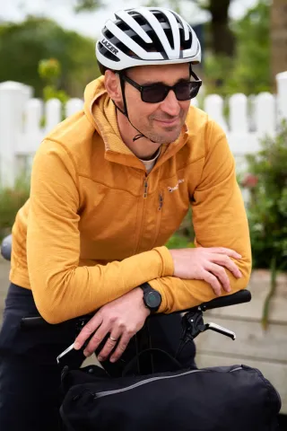 A cyclist in an orange top and white helmet resting on a bike