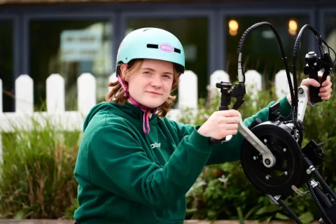 A young cyclist in a green top checking a phone beside a bike