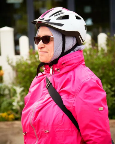 A cyclist in a pink jacket and white helmet looking to the side