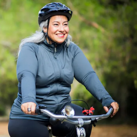A smiling woman wearing a cycling helmet, riding her bike outdoors.