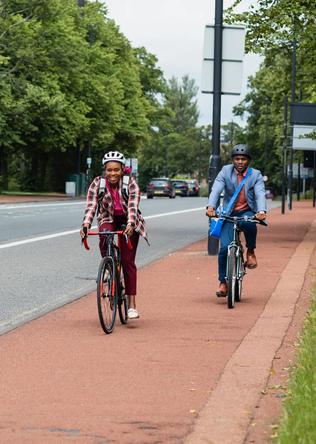 Two adults cycling with confidence along a protected cycle lane beside a tree-lined road.