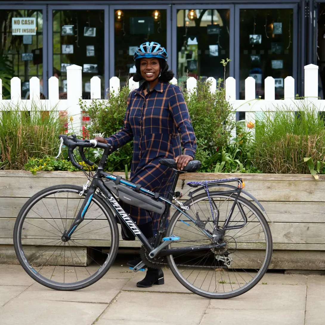 An adult standing with their bicycle on a paved street, smiling.
