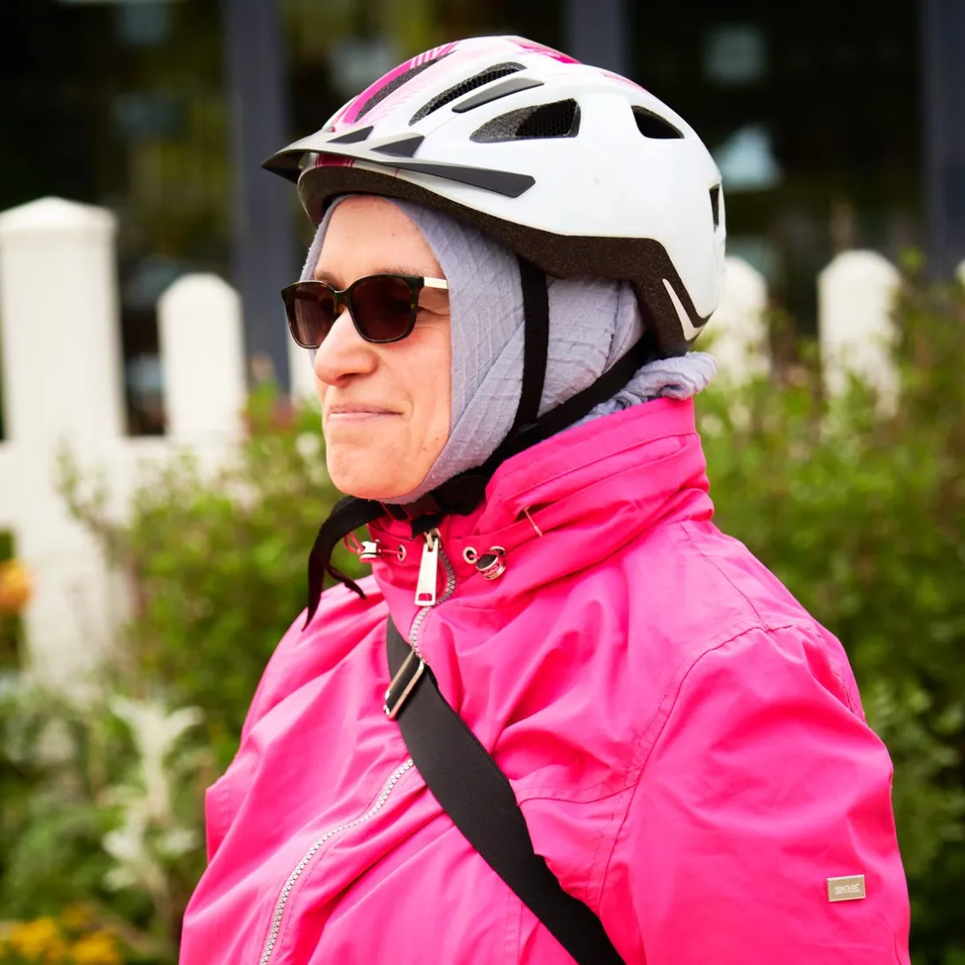 An adult in a bright pink cycling jacket, helmet and sunglasses, ready to ride.